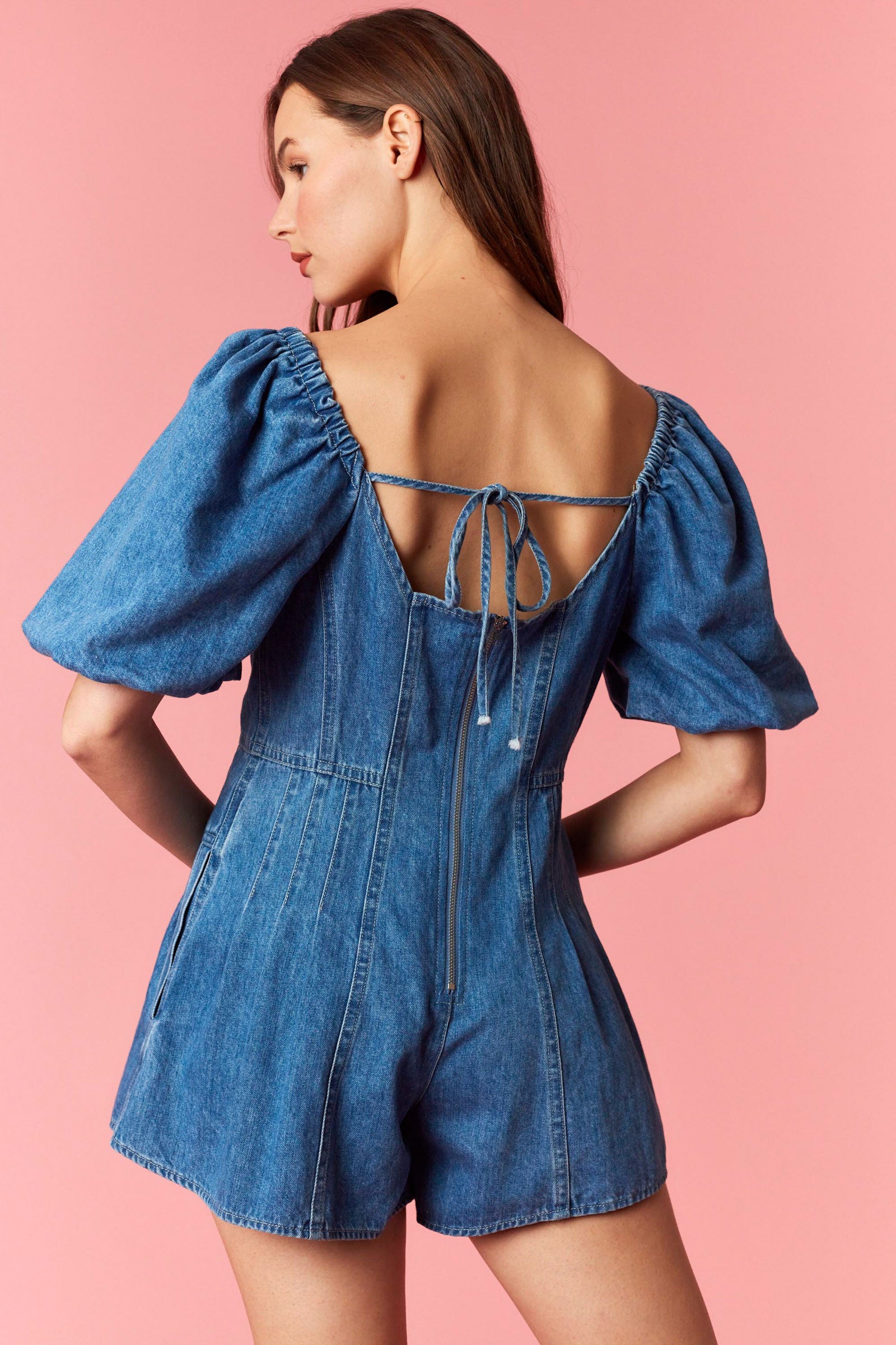 Woman wearing a game day denim romper with bubble sleeves and pleated detail with tie back