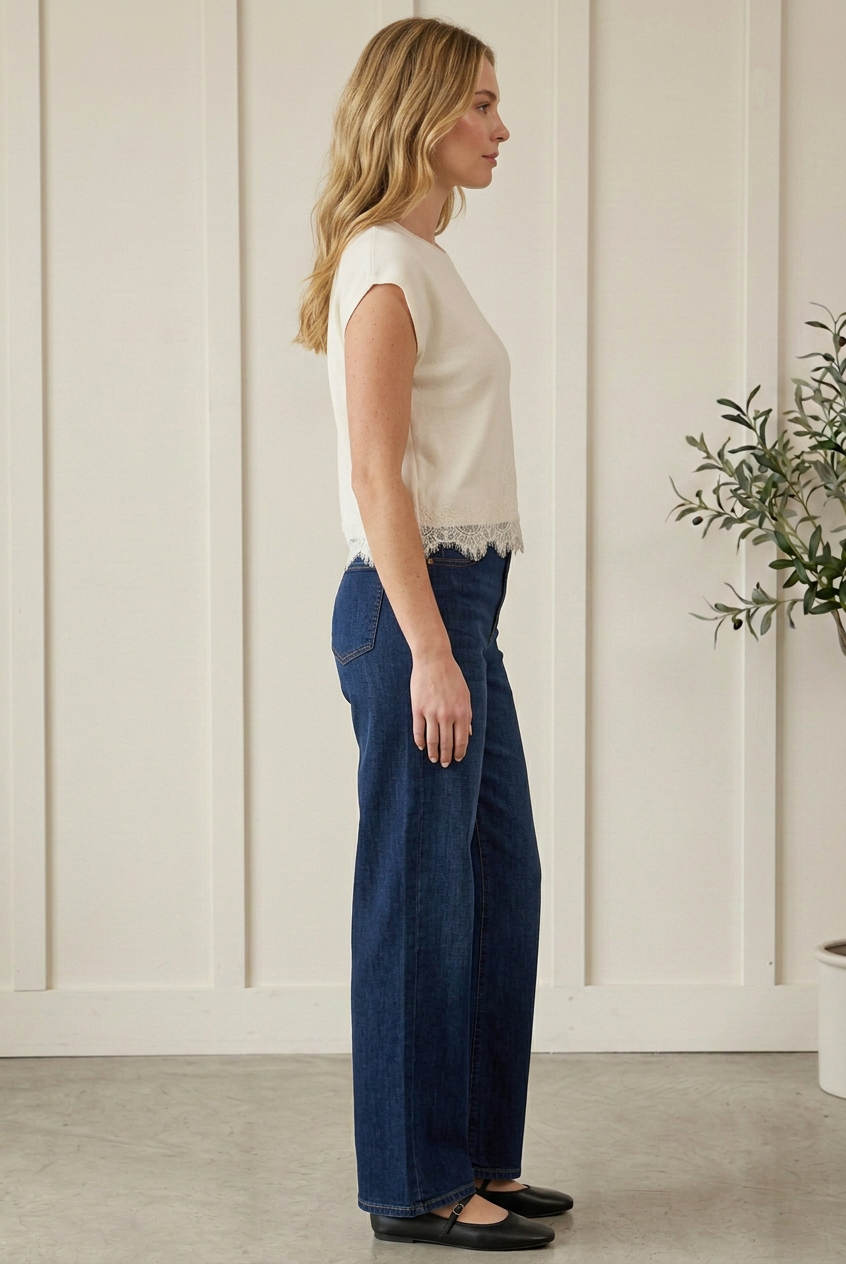 Side view of cream sweater top showing cap sleeves, an easy silhouette and lace trim hem, paired with dark jeans.