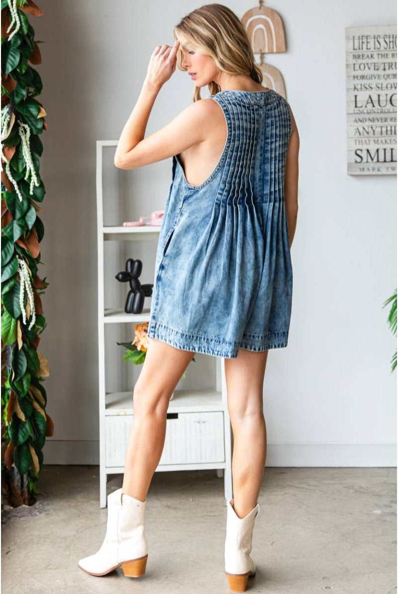 Woman wearing a stylish sleeveless denim romper with deep V-neckline, front pleats, and tie detail at the bust; perfect trendy summer outfit for women from a boutique collection.