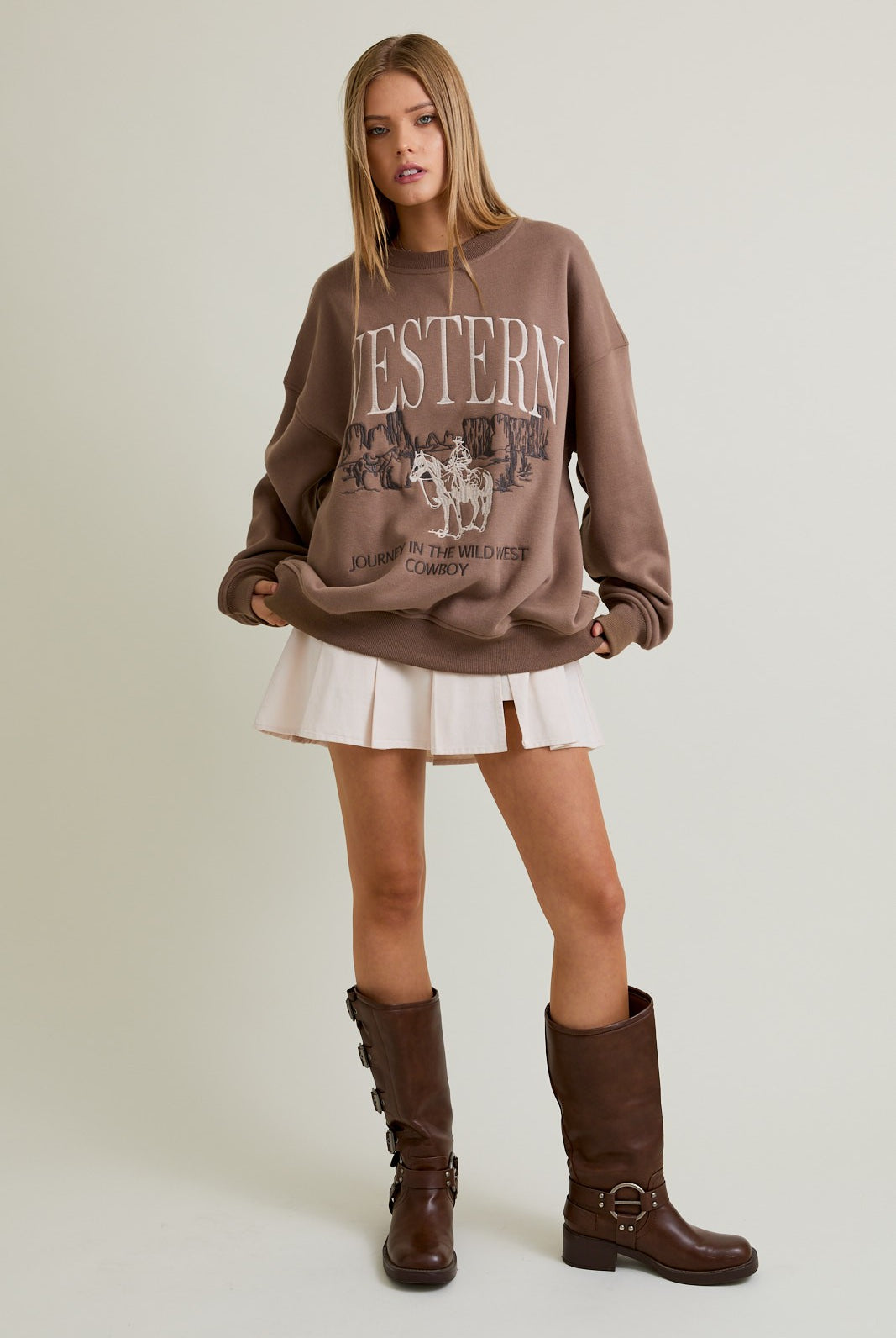 Woman wearing a mocha oversized crewneck sweatshirt with “Western” embroidery and a cowboy graphic