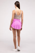 Woman wearing a pink ruffle hem tennis skirt with hidden inner pockets, styled for activewear and summer fashion.