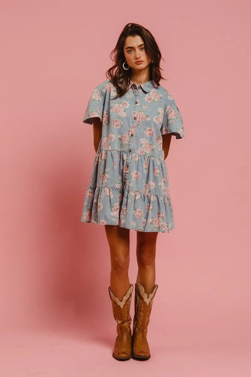 Model wearing the Wild Rose Shirt Dress in soft blue with rose print, flutter sleeves, and tiered ruffle skirt