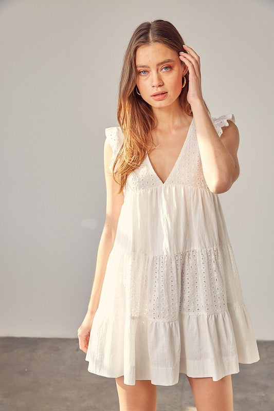 A stylish woman poses in a flattering V-neck eyelet dress, showcasing its delicate detailing and breezy silhouette. The dress flows effortlessly as she moves, exuding feminine charm and elegance. She pairs it with strappy heels and subtle jewelry, making it the perfect outfit for brunch, a summer date, or a special occasion. The lightweight fabric and airy design create a timeless, effortlessly chic look.