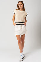 Model wearing a sleeveless round neck crop top with ruffle sleeves and color contrast trim, styled with high-waisted jeans — perfect for casual summer outings or brunch dates.