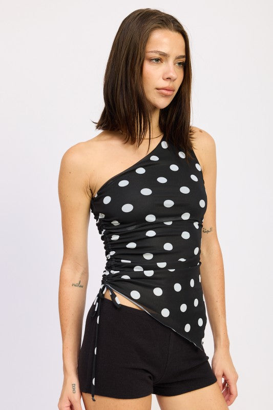 Black one-shoulder top with white polka dots worn by a person on a plain background side view
