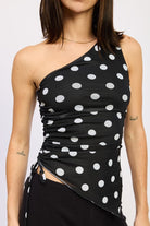 Black one-shoulder top with white polka dots worn by a person on a plain background close up