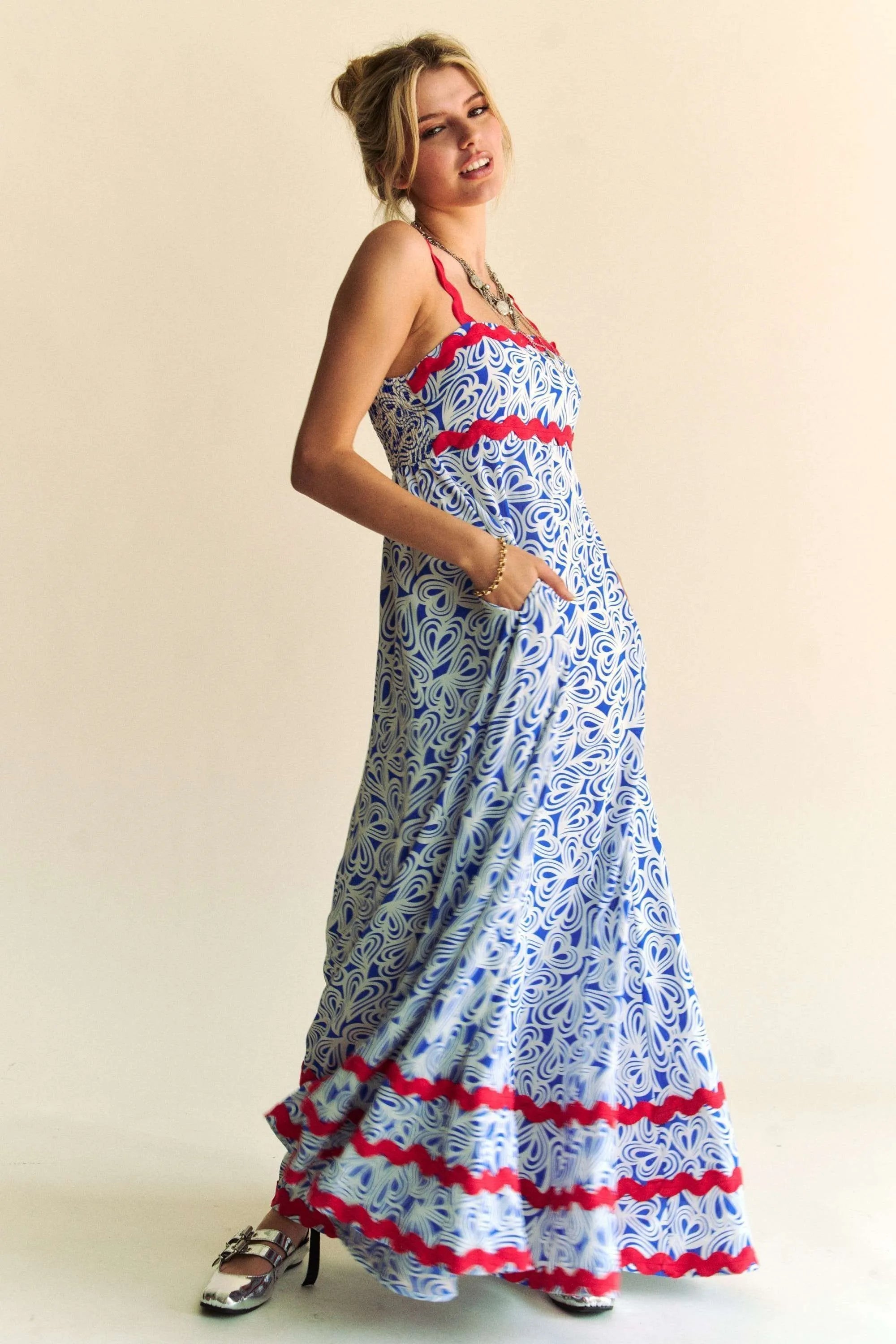 Woman wearing a patriotic-themed maxi dress with a blue and white heart pattern, red scalloped trim, and smocked bodice