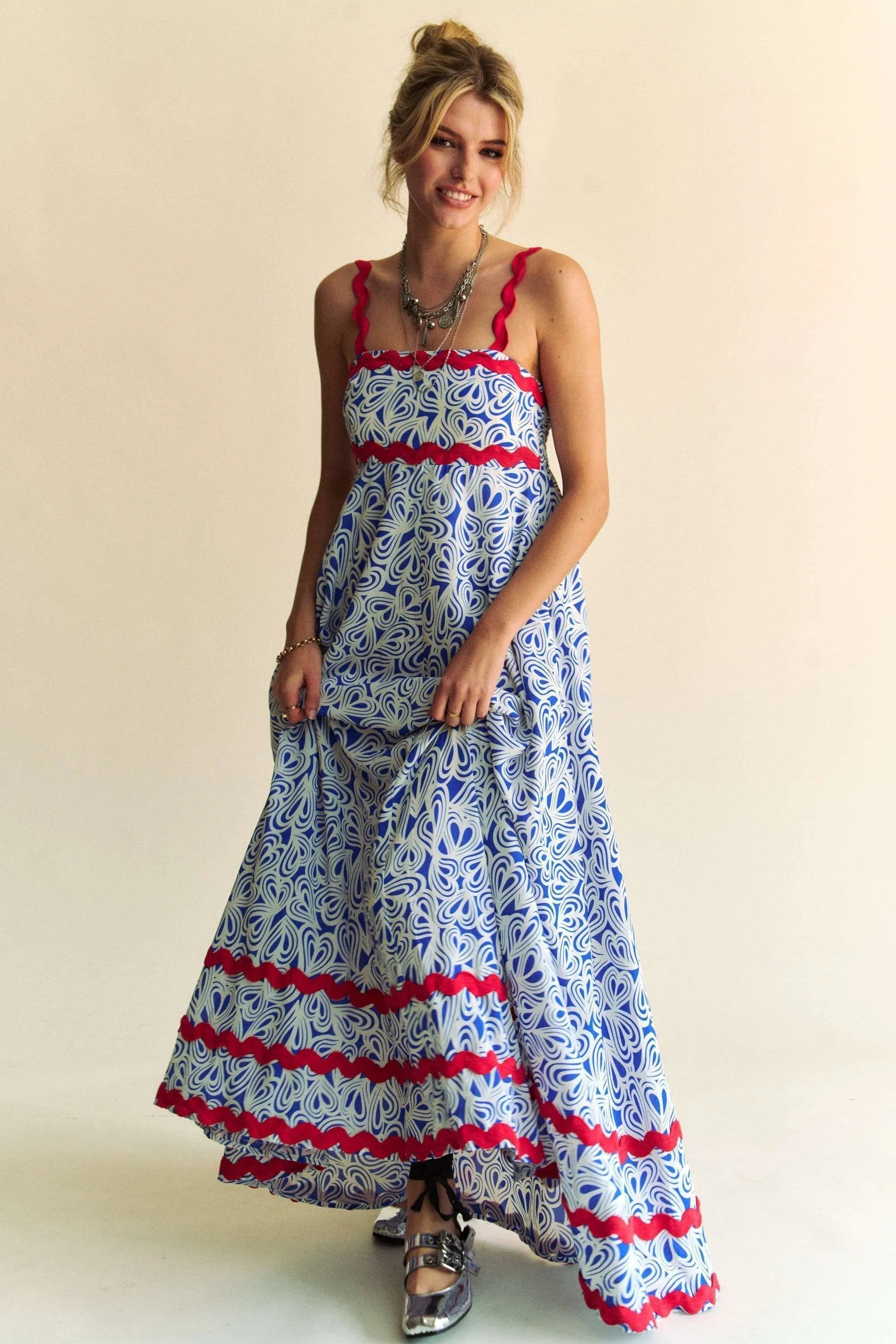 Woman wearing a patriotic-themed maxi dress with a blue and white heart pattern, red scalloped trim, and smocked bodice