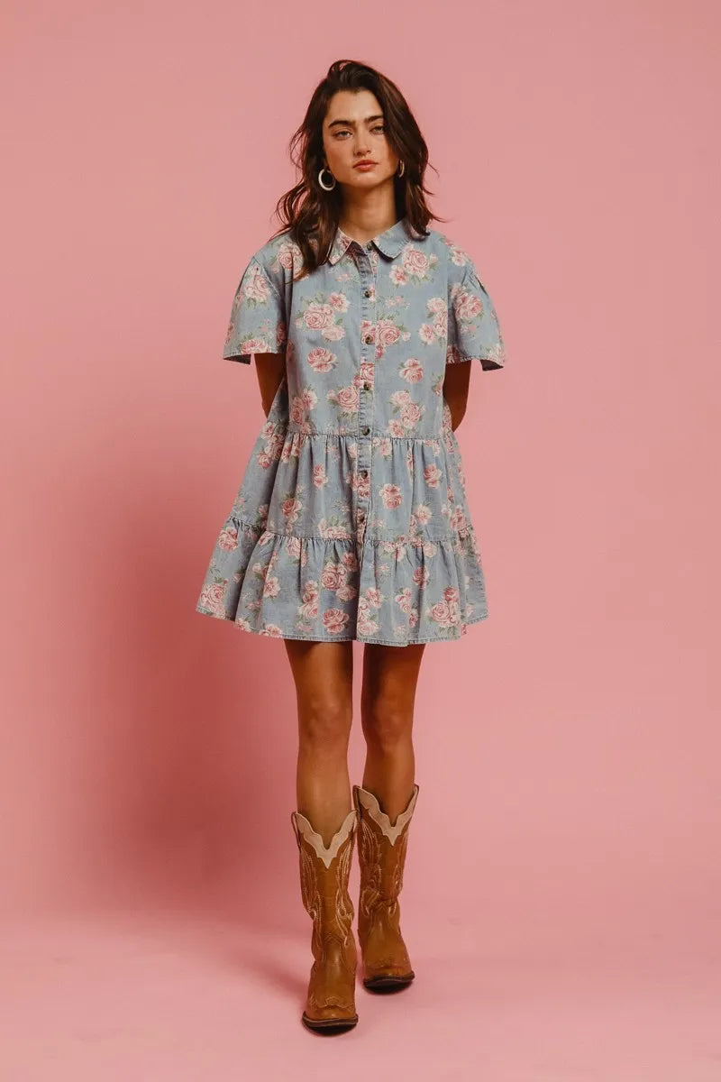 Model wearing the Wild Rose Shirt Dress in soft blue with rose print, flutter sleeves, and tiered ruffle skirt