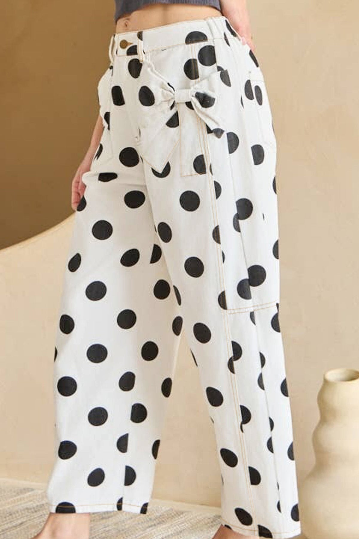Person wearing white pants with black polka dots in a minimal indoor setting.