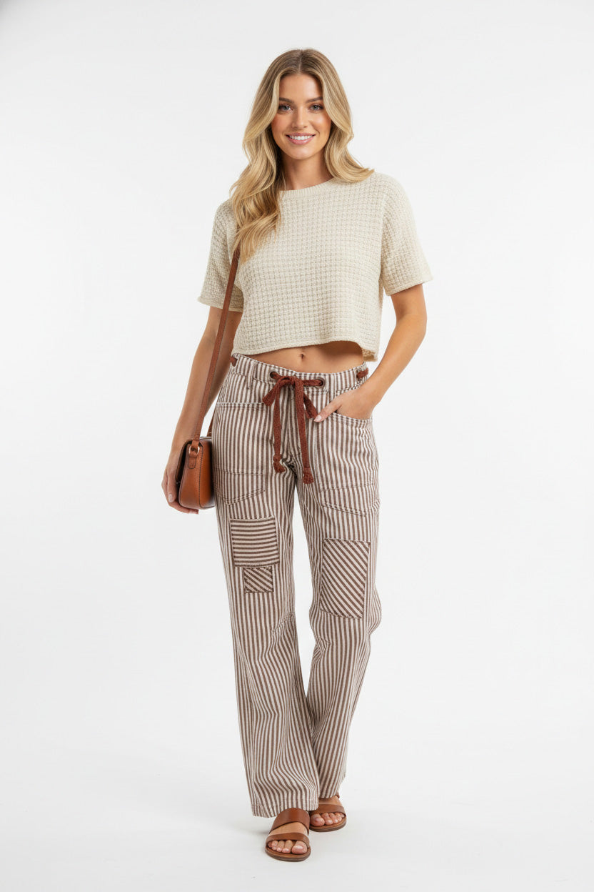 Woman wearing brown and cream striped barrel pants with drawstring waist and cargo pockets, styled with cropped cream top