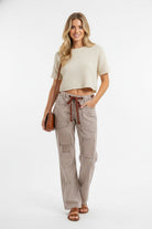 Woman wearing brown and cream striped barrel pants with drawstring waist and cargo pockets, styled with cropped cream top
