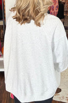 A woman viewed from behind wearing an oversized light heather gray raglan sweatshirt and black pants in a retail store setting.
