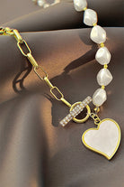 Pearl bracelet with gold chain and heart-shaped charm on a brown surface