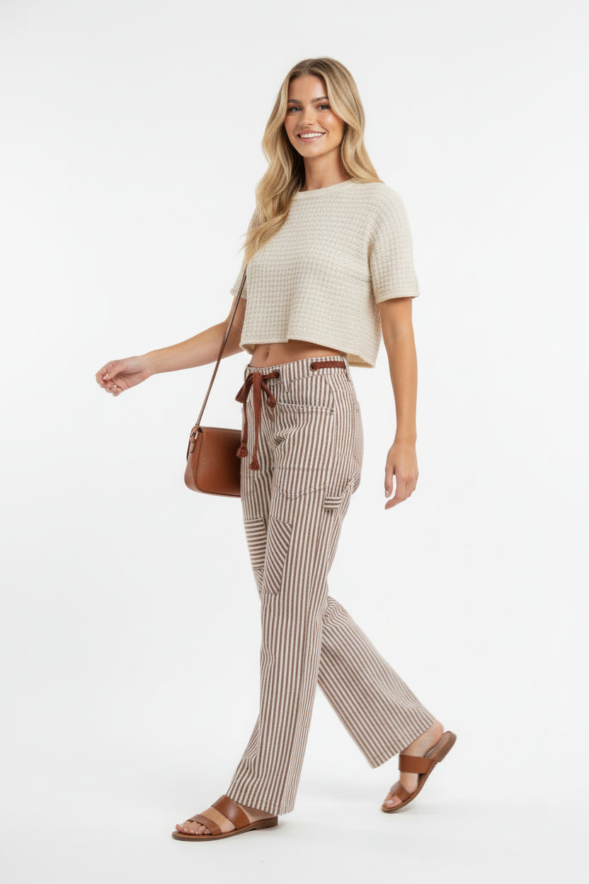 Woman wearing brown and cream striped barrel pants with drawstring waist and cargo pockets, styled with cropped cream top side view