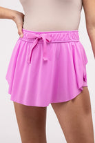 Woman wearing a pink ruffle hem tennis skirt with hidden inner pockets, styled for activewear and summer fashion.