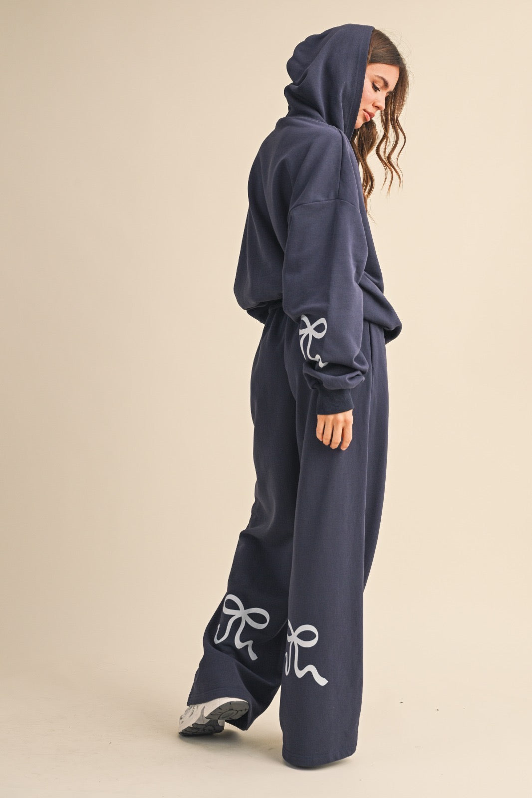 Model wearing navy wide-leg sweatpants with light blue bow details, styled with a matching navy hoodie.