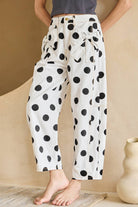 Person wearing white pants with black polka dots in a minimal indoor setting.