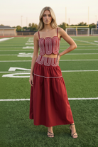 Blonde model wearing crimson red lace trim crop top and tiered maxi skirt set - front facing on football field