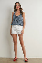 Woman wearing a denim peplum top and white shorts against a plain background