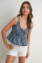 Woman wearing a denim peplum top and white shorts on a plain background