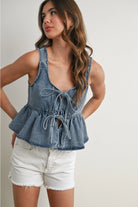 Woman wearing a denim peplum top and white shorts on a plain background