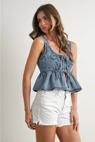Woman wearing a denim peplum top and white shorts on a plain background
