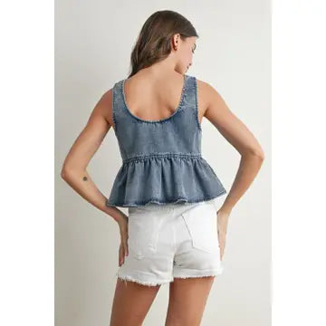 Woman wearing a denim peplum top and white shorts on a plain background