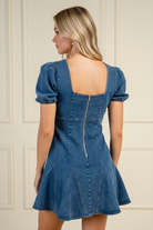 Back view of medium wash denim mini dress showing back zipper and godet hem panel detail, blonde model