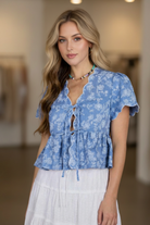 Floral embroidered V-neck peplum top from Thread Bar Boutique with front tie details, lightweight woven fabric, and a flattering ruffle hem. Elegant boutique top for women seeking feminine everyday fashion.