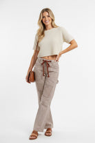 Woman wearing brown and cream striped barrel pants with drawstring waist and cargo pockets, styled with cropped cream top perfect fit