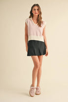 A model wearing a pink striped sleeveless knit vest with a V-neckline and ribbed hem