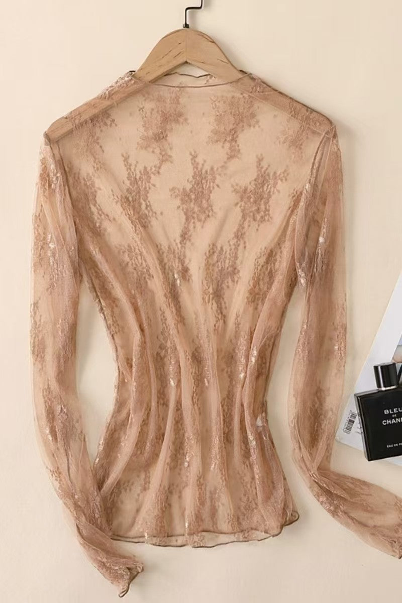 Sheer beige lace top on a hanger against a beige wall.