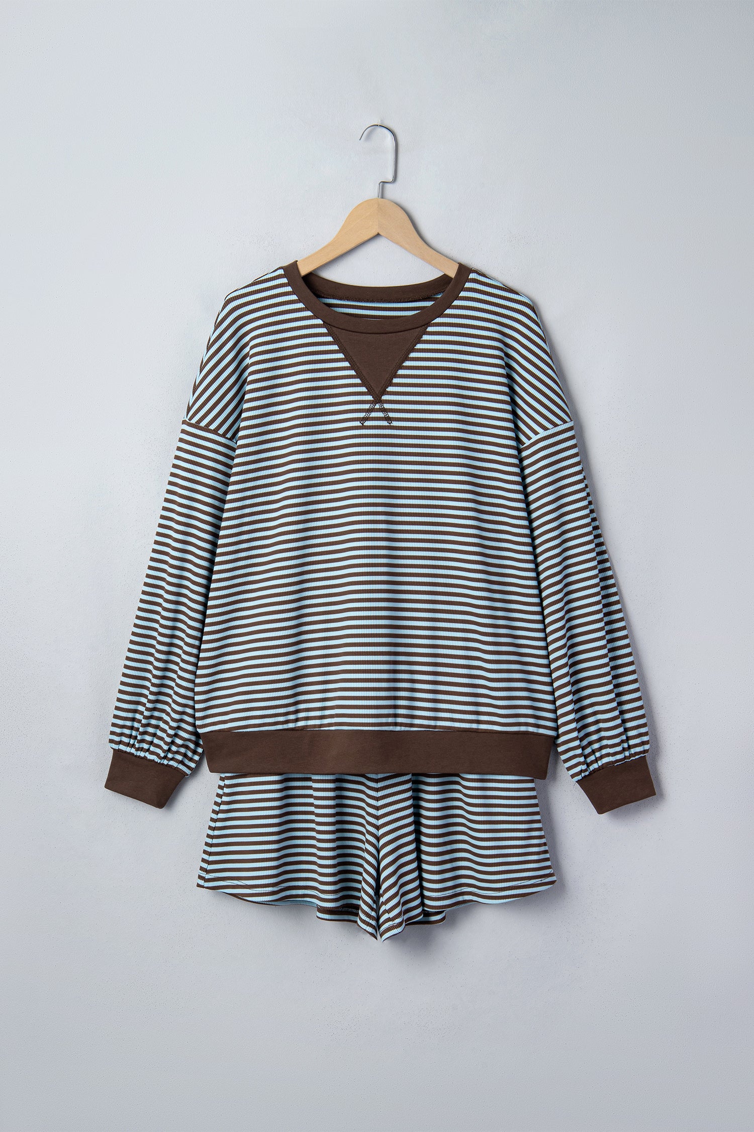 A long-sleeve striped top with brown ribbed trim, hanging on a wooden hanger against a light gray wall.
