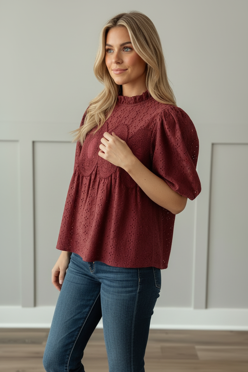 Three-quarter half-body close-up of cranberry eyelet blouse showing short voluminous puff sleeves, crochet medallion embroidery detail, ruffled neckline, and lightweight 100% cotton eyelet fabric
