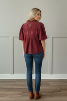 Back view of cranberry burgundy eyelet blouse showing ornate crochet medallion back detail, button keyhole closure at ruffled mock neckline, and short puff sleeves