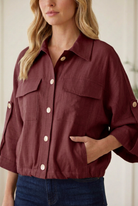 Close-up of burgundy utility jacket showing pale front buttons, flap chest pockets, side pocket and woven fabric texture