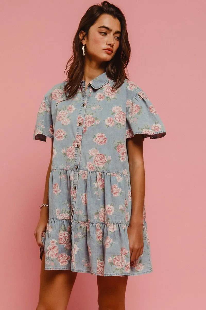 Model wearing the Wild Rose Shirt Dress in soft blue with rose print, flutter sleeves, and tiered ruffle skirt