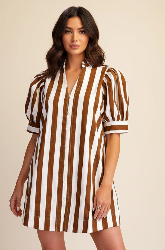 A woman modeling a brown and white vertically striped short-sleeve button-up dress with puff sleeves, photographed against a plain beige studio background.