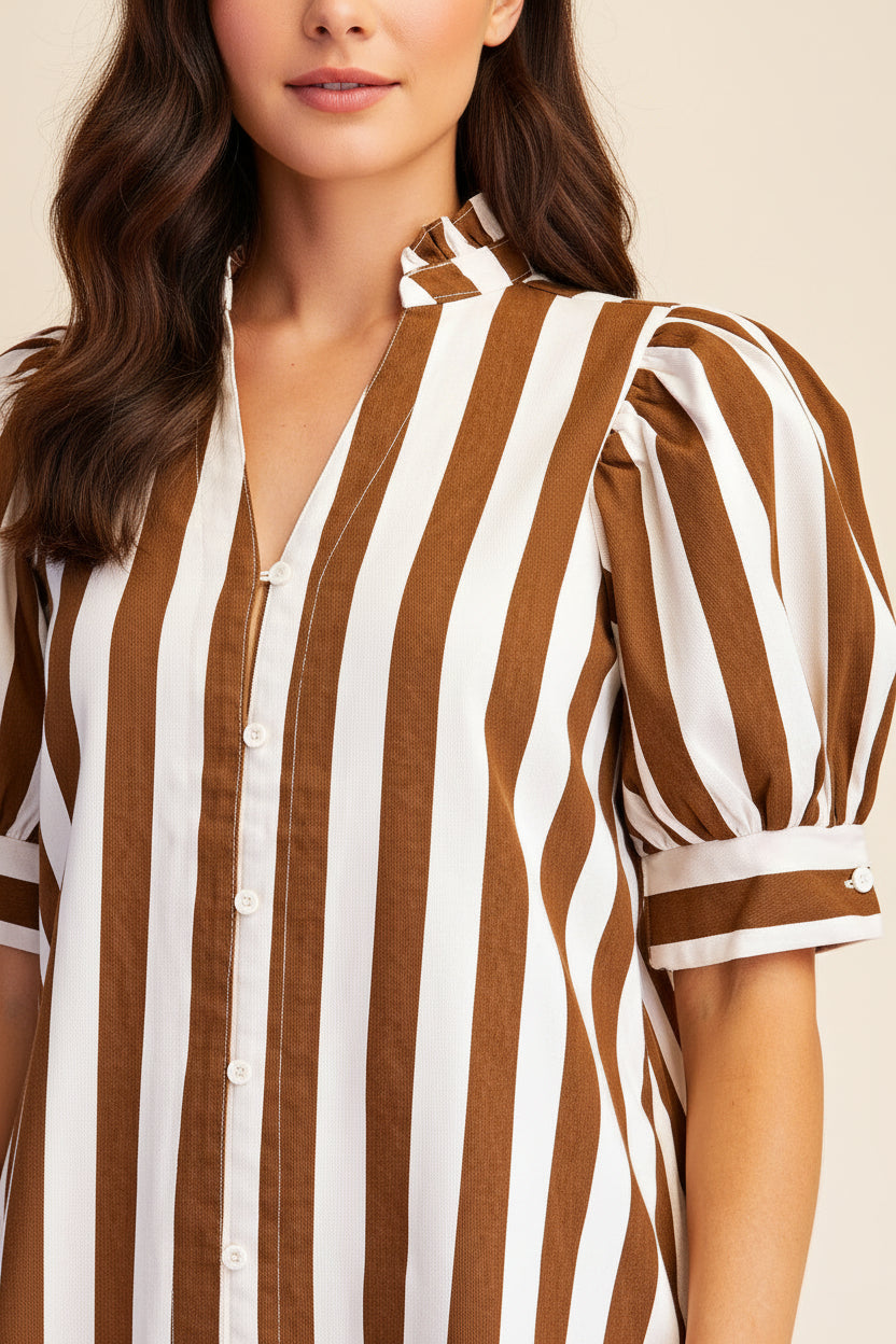 A close-up of a woman wearing a brown and white vertically striped button-up shirt dress with puff sleeves and a tie-neck detail, set against a plain beige background.