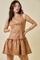 Woman wearing a camel-colored suede mini dress featuring a drop waist with bow ties, sleeveless design, and a back zipper closure. The dress has a soft, structured texture and a flattering A-line silhouette, styled for a chic fall look.