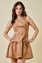 Woman wearing a camel-colored suede mini dress featuring a drop waist with bow ties, sleeveless design, and a back zipper closure. The dress has a soft, structured texture and a flattering A-line silhouette, styled for a chic fall look.