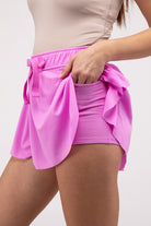 Woman wearing a pink ruffle hem tennis skirt with hidden inner pockets, styled for activewear and summer fashion.