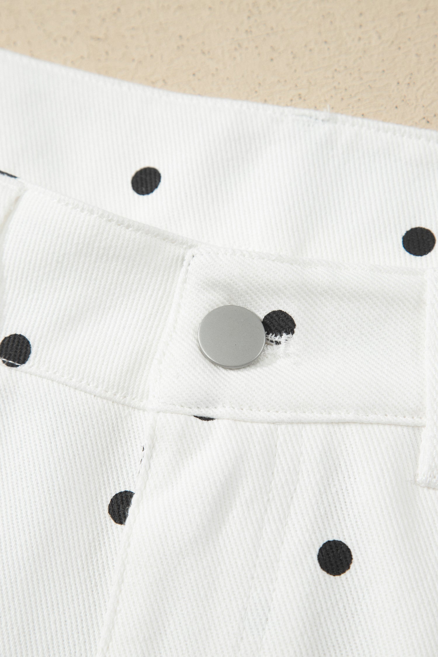 White fabric with black polka dots and a metal button 