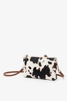 Cow print handbag with brown strap on a white background