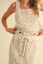 A model wearing a cream-colored crochet crop top and matching maxi skirt with a tie waist and built-in slip.
