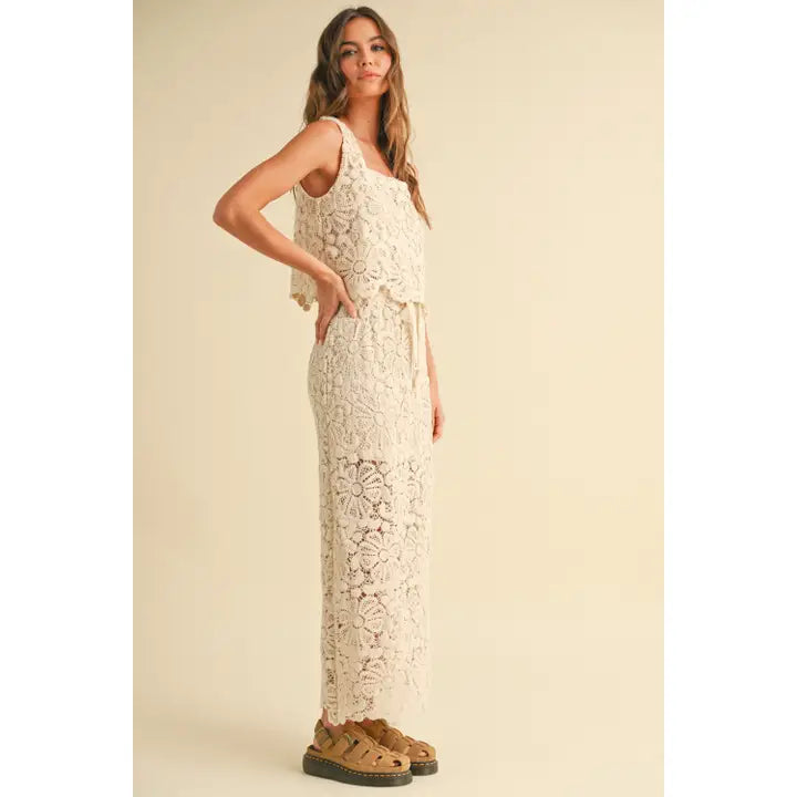 A model wearing a cream-colored crochet crop top and matching maxi skirt with a tie waist and built-in slip, 