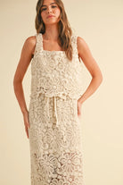 A model wearing a cream-colored crochet crop top and matching maxi skirt with a tie waist and built-in slip