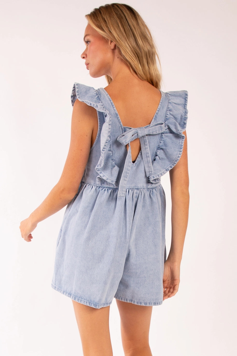  A stylish denim romper featuring delicate ruffle sleeves, a scoop neckline, and a tie-back detail. Designed with a relaxed fit in lightweight denim, this romper includes side pockets for a blend of practicality and effortless summer style. Perfect for casual outings and warm-weather adventures.