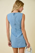 Woman wearing light blue denim sleeveless mini dress with diagonal bow tie details and exposed seam accents  zipper back